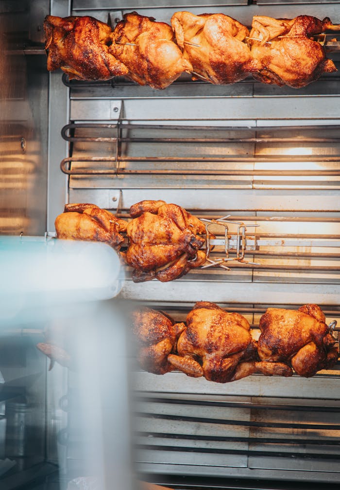about-01 Mouthwatering rotisserie chicken cooked to perfection on a grill spit in a cozy indoor setting.